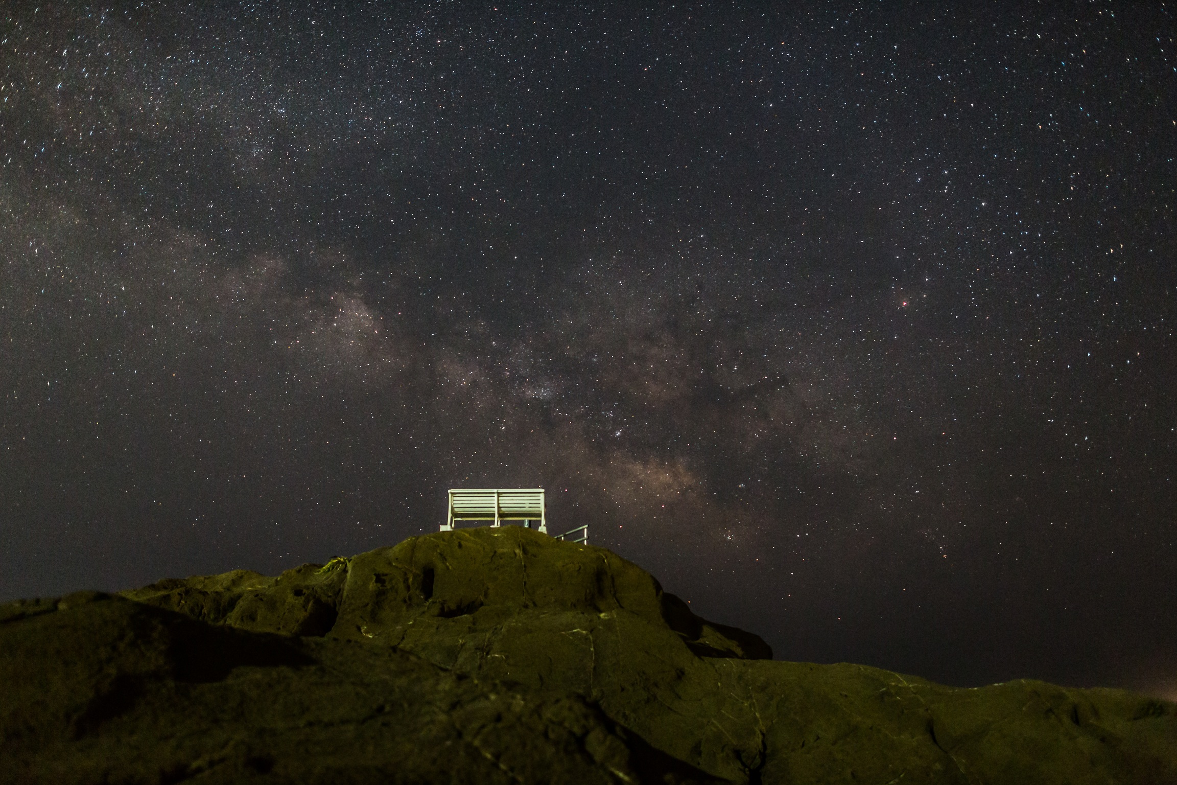 南房総市白浜で撮影された、岩場の白いベンチと満天の星空